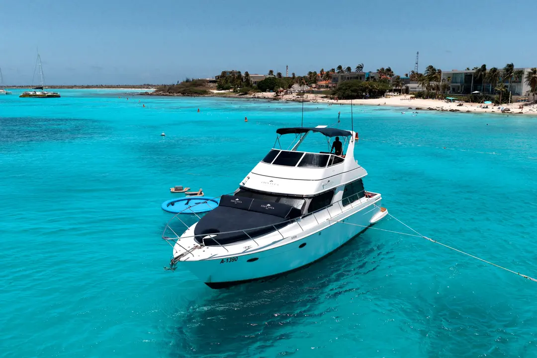 Drone view of Eden Luca Blue at anchor off an Aruba beach, navy bow lounge over turquoise water