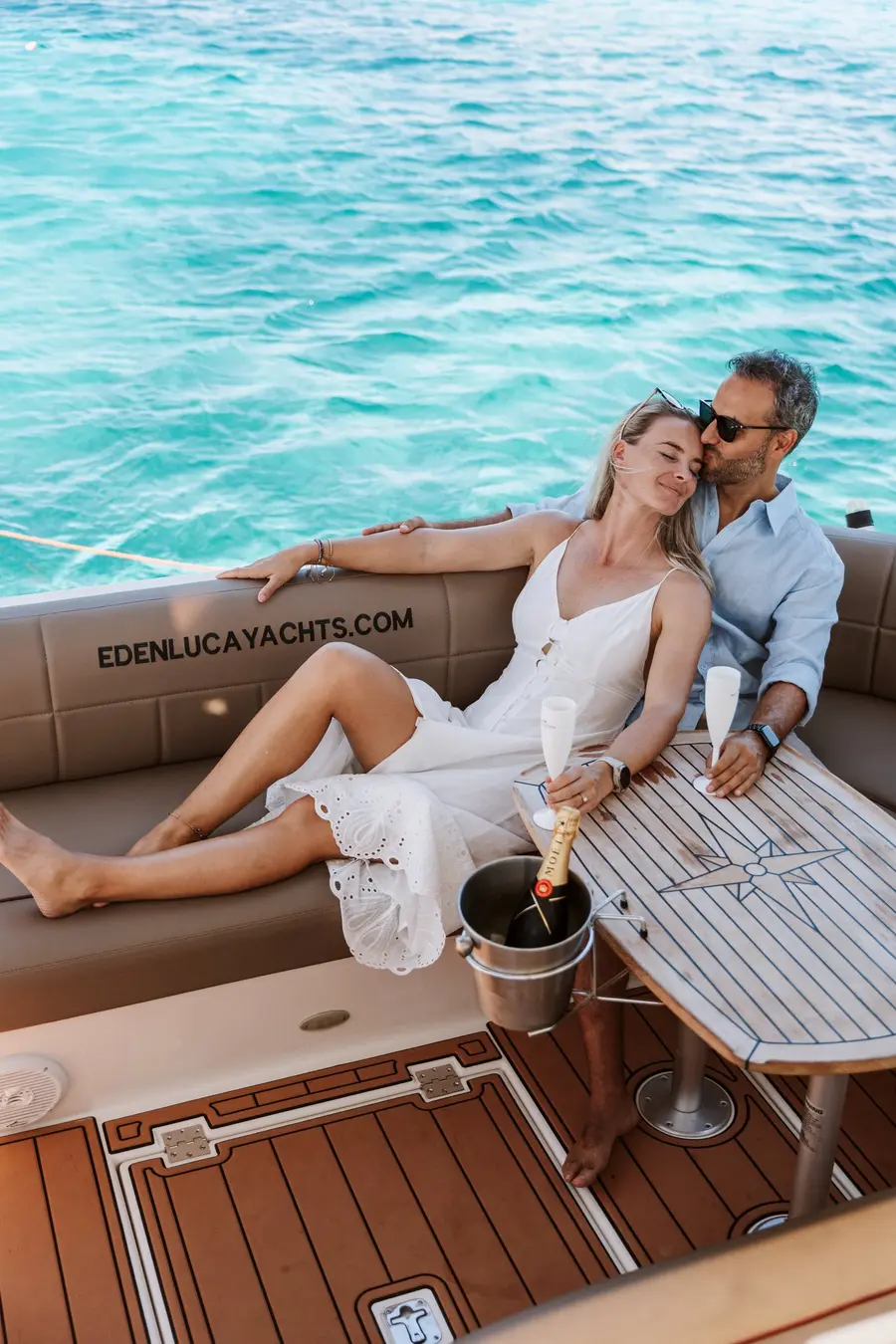 Couple lounging with champagne on the aft deck of Eden Luca Red, turquoise water behind